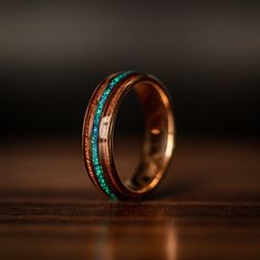 a wedding band that has been made with gold and green inlays, on a wooden surface