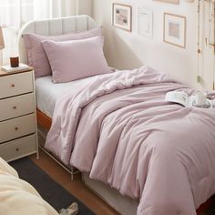 a bed with pink comforter and pillows in a bedroom next to a white dresser