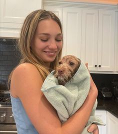 a woman holding a small dog wrapped in a towel while standing in a kitchen with white cabinets