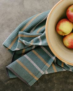 a bowl filled with apples sitting on top of a blue and yellow cloth next to a napkin