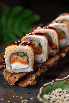 sushi rolls with sauce and cucumber are on a piece of driftwood