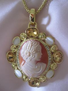 AMEDEO Hand Carved Cameo Necklace  A really spectacular show stopping piece from AMEDEO.  It features a large carved shell cameo in an ornate gold plated necklace. Surrounding the cameo are sparkling white crystals. Framing this elegant "portrait" is a wide oval frame of large citrine rhinestones and moonstone glass cabochons.  Gold chain measures approx. 17" with a 2.25 inch enhancer . The bale is also covered with white crystals. The amazing cameo pendant measures approx. 2.25 by 2.25 inches. Luxury Gold Cameo Jewelry, Luxury Cameo Pendant Jewelry, Luxury Gold Cameo Necklace, Luxury Oval Cameo Necklace, Luxury Cameo Medallion Jewelry, Exquisite Cameo Jewelry For Gift, Exquisite Cameo Jewelry For Formal Occasions, Collectible White Cameo Jewelry, Exquisite Gold Necklace For Collectors