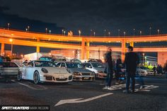 a group of cars parked in a parking lot next to an overpass at night