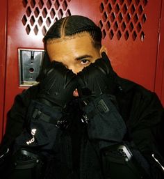 a man in black jacket covering his face with both hands while standing next to red door