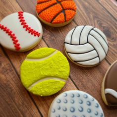 four decorated cookies with different designs and colors on a wooden table, including one tennis ball, the other as a volleyball