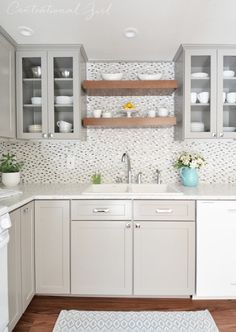 a kitchen with white cabinets and wooden shelves on the wall next to an area rug