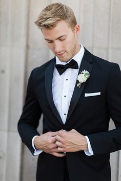 a young man in a tuxedo adjusts his bow tie while looking down