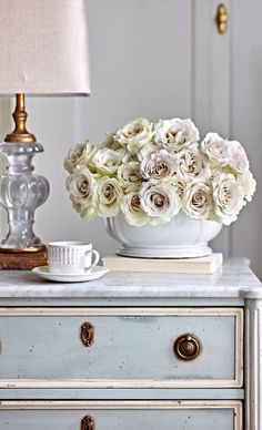 a white vase filled with flowers sitting on top of a table next to a lamp