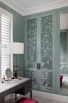 a desk with a lamp and mirror on it in front of a green wallpapered closet