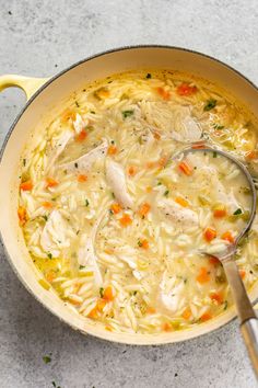 a pot filled with chicken noodle soup on top of a white counter next to a spoon