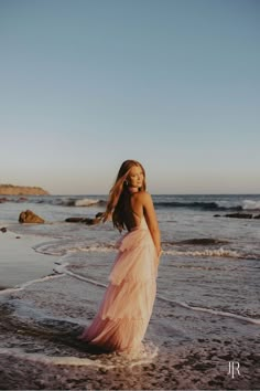 a woman in a pink dress standing on the beach