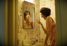 a woman standing in front of a bathroom mirror brushing her teeth and looking at herself in the mirror