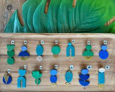 a wooden board with several different colored earrings on it and a large green leaf in the background