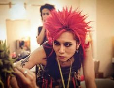 a woman with red hair and piercings on her head sitting in front of a plant