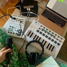 a person sitting in front of a laptop with headphones on, next to a keyboard and microphone