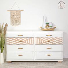 a white dresser with gold handles and drawers in front of a wall hanging on the wall