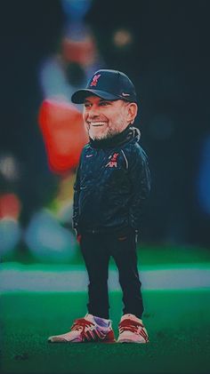 a man with a beard wearing a baseball cap and black pants standing in the grass