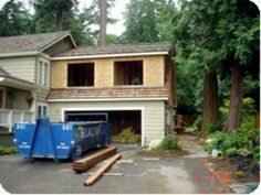 a house being built with blue trash cans in front of it and trees around the house