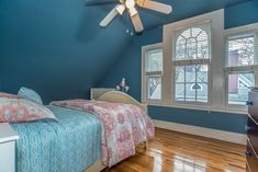 a bedroom with blue walls and wooden floors has a ceiling fan in the corner that matches the bed