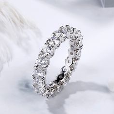 a diamond ring on top of a white table with some feathers in the back ground