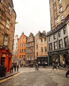 people are walking around in the middle of an old city street with tall buildings on either side