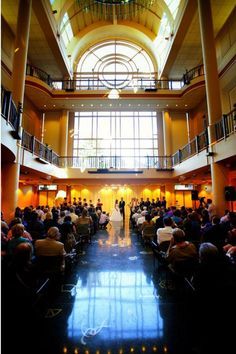 a wedding ceremony in the atrium of a building with people sitting on pews and looking at each other