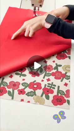 someone is using an apple watch to sew on a red sheet of paper with flowers