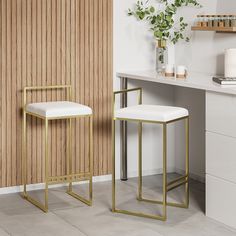 two white stools sitting next to each other in front of a counter with a potted plant on it