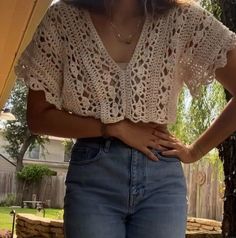 a woman standing in front of a tree with her hands on her hips, wearing jeans and a crocheted top