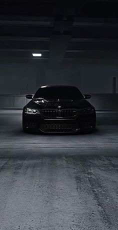 a black car is parked in an empty parking garage with its lights on at night