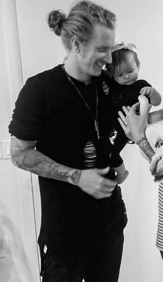 a man holding a baby in his arms while standing next to two other people with tattoos on their arms