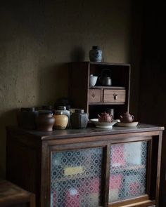 an old wooden cabinet with bowls and cups on it's glass doors, in a dark room