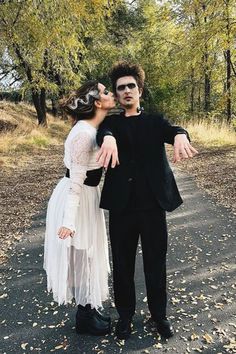 a man and woman dressed up in costumes standing on a road with trees behind them