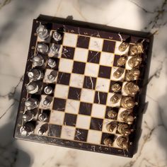 a marble chess board with gold and silver pieces on it's sides, sitting on a marble surface