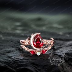 a ring with a red stone in the center on top of a black rock,