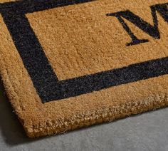 a door mat with the letter n on it is laying on a gray surface and has a black border