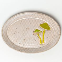 a ceramic plate with two mushrooms on the front and one mushroom on the back, sitting on a white surface