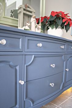 a blue dresser with red poinsettia flowers on top and a mirror in the background