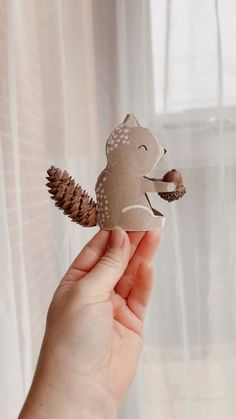 a hand holding up a paper cutout of a squirrel with pine cones on its tail