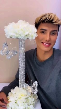 a young man sitting next to a bouquet of white flowers and butterfly brooches