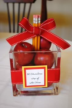 an apple and pencils in a clear container with a red ribbon tied around it