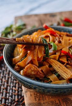 a bowl filled with noodles and vegetables on top of a woven place mat next to chopsticks