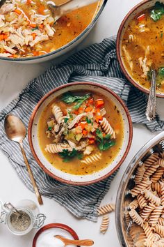 two bowls filled with pasta and chicken noodle soup on top of a white table