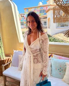 a woman in a white dress is holding a blue handbag and posing for the camera