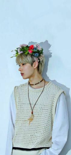 a woman with flowers in her hair standing against a white wall wearing a flower crown