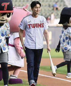 a man walking across a baseball field with mascot behind him and another person holding a bat