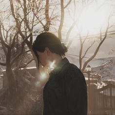 a person standing in front of trees with the sun shining down on them and snow covered ground