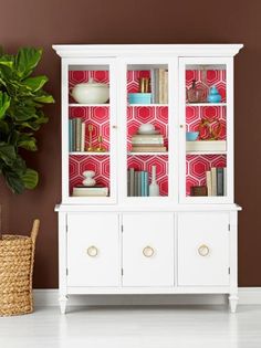 a white china cabinet with books and vases on it next to a potted plant