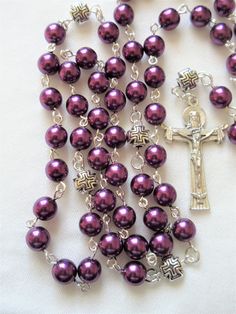 This plum purple Catholic rosary is made with larger 8mm Czech glass pearls. It has a Holy Trinity crucifix and a Miraculous medal connector. The Pater beads are 8mm puffed pewter cross beads. All of the silver plated wires are hand turned. The body of the rosary is 30 inches around and has a 5.5 inch cross drop. This rosary will be slipped into a velvet bag and shipped in a bubble mailer. Cross Beads, Catholic Rosary, The Rosary, Rosary Catholic, Miraculous Medal, Bubble Mailer, Holy Trinity, Plum Purple, Velvet Bag