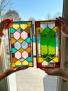 two people holding up stained glass windows in front of a door with the window open